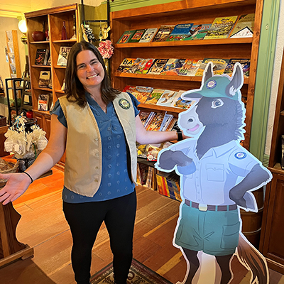 Image of Kristin wearing Parks uniform standing next to a donkey cutout. She is in the Visitors Center.